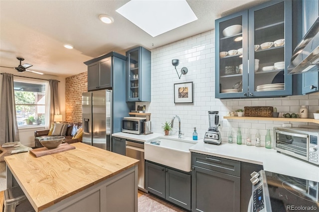 kitchen featuring backsplash, glass insert cabinets, stainless steel appliances, and a sink