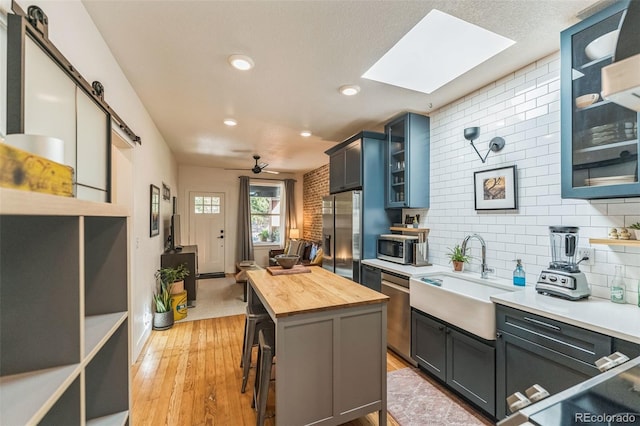 kitchen featuring stainless steel appliances, butcher block counters, a sink, backsplash, and a center island