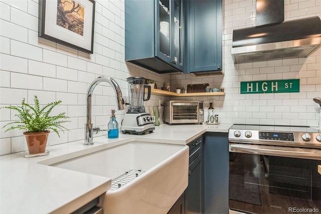 kitchen featuring tasteful backsplash, wall chimney exhaust hood, blue cabinets, stainless steel range with electric cooktop, and a sink