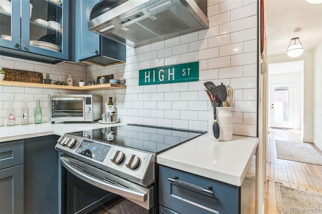 kitchen with blue cabinetry, wall chimney exhaust hood, stainless steel electric range, and backsplash