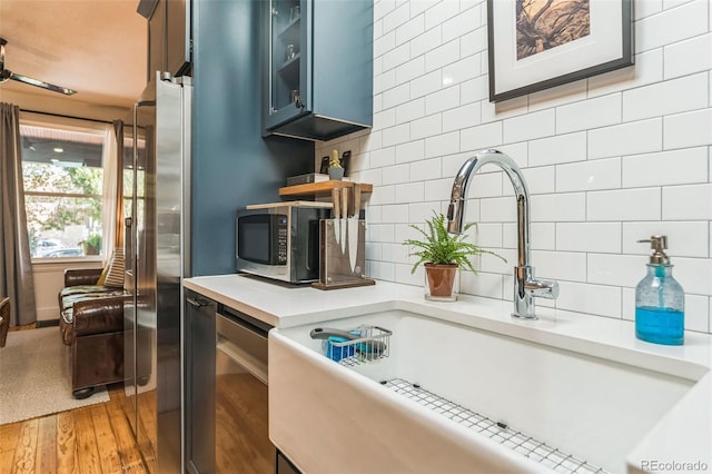 kitchen featuring stainless steel appliances, tasteful backsplash, light countertops, light wood-style flooring, and glass insert cabinets