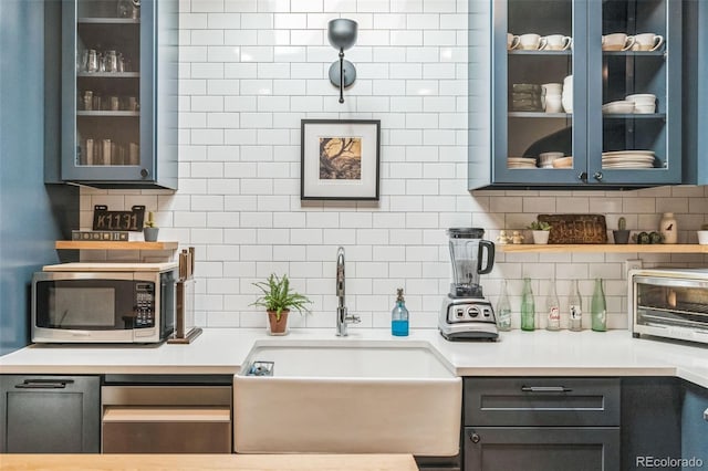 kitchen featuring tasteful backsplash, light countertops, stainless steel microwave, and a sink