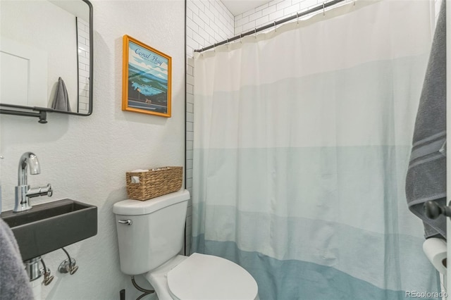 full bathroom with a textured wall, a shower with curtain, a sink, and toilet