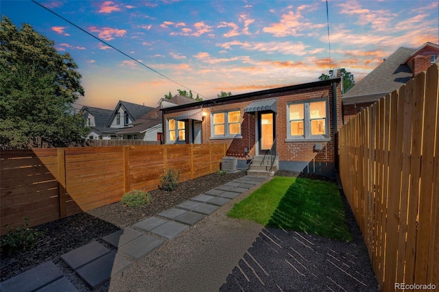 view of front of home with entry steps, a fenced backyard, cooling unit, and brick siding