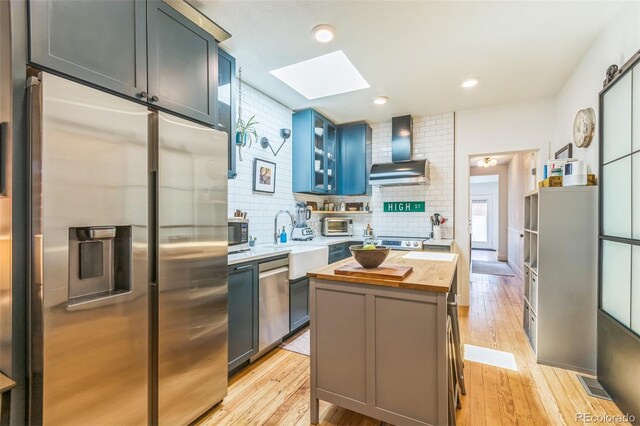 3329 N High St, Denver, CO 80205 - kitchen featuring a sink, stainless steel appliances, a skylight, butcher block counters, and wall chimney exhaust hood