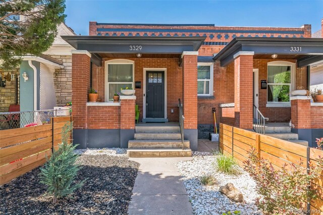 3329 N High St, Denver, CO 80205 - doorway to property with a porch, fence, and brick siding