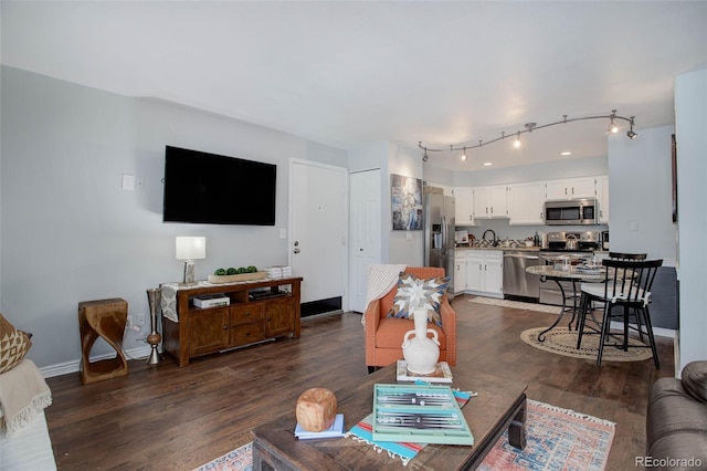 living room with rail lighting, dark wood-type flooring, and sink