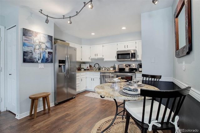 kitchen with appliances with stainless steel finishes, dark hardwood / wood-style floors, sink, white cabinets, and track lighting