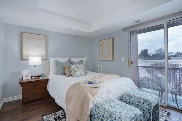 bedroom featuring access to exterior, a tray ceiling, and dark wood-type flooring