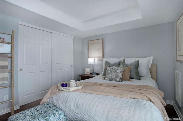 bedroom featuring dark hardwood / wood-style flooring, a raised ceiling, and a closet