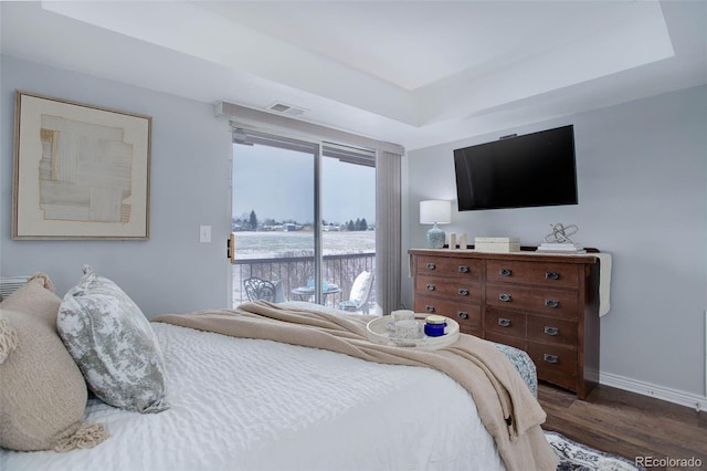 bedroom featuring a raised ceiling, dark hardwood / wood-style floors, and access to outside