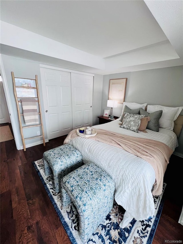 bedroom featuring a tray ceiling, dark wood-type flooring, and a closet