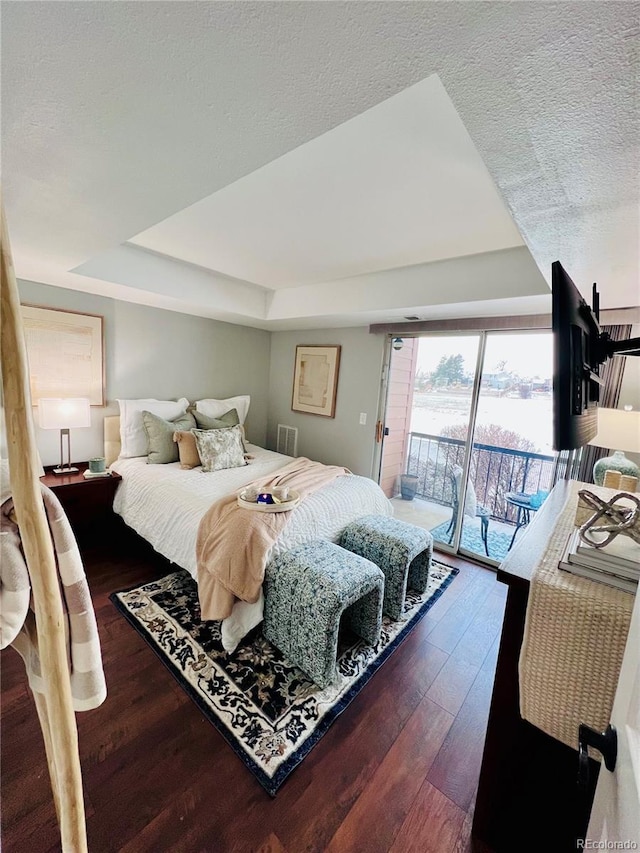 bedroom featuring dark wood-type flooring, access to outside, a textured ceiling, and a tray ceiling