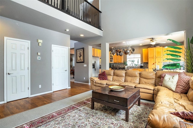 living room with ceiling fan with notable chandelier, a towering ceiling, and hardwood / wood-style flooring