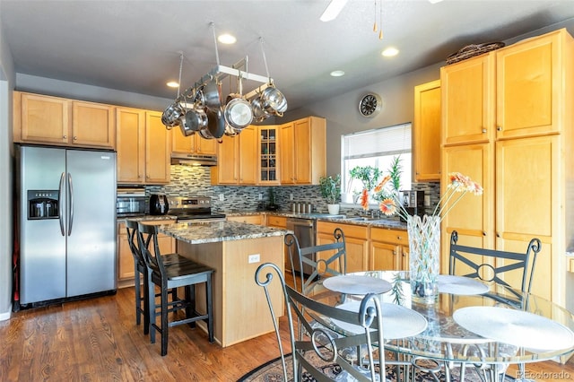 kitchen featuring tasteful backsplash, stainless steel appliances, dark wood-type flooring, stone countertops, and a center island