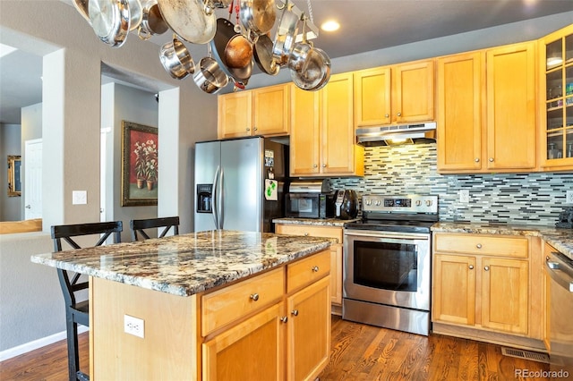 kitchen featuring appliances with stainless steel finishes, dark hardwood / wood-style flooring, light stone counters, a center island, and a breakfast bar area