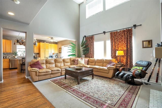 living room featuring hardwood / wood-style flooring, ceiling fan with notable chandelier, and a towering ceiling