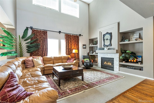 living room featuring a fireplace, built in features, hardwood / wood-style floors, and a high ceiling