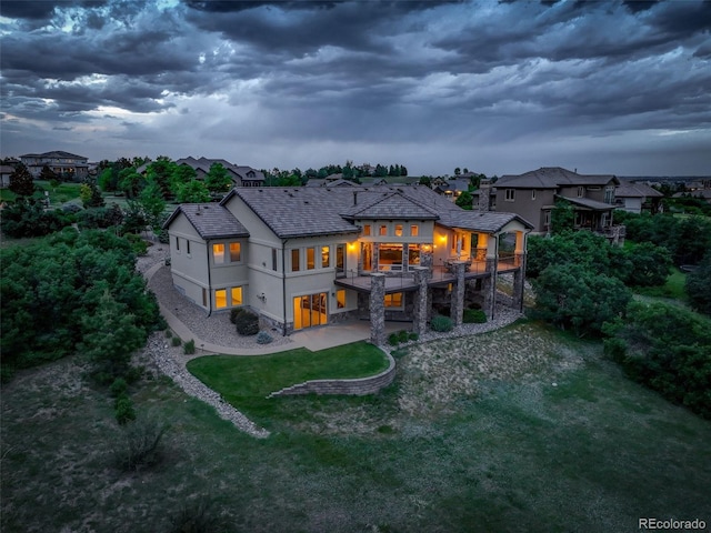 back house at dusk featuring a lawn, a patio, and a wooden deck