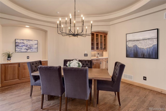 dining room with light hardwood / wood-style flooring, a raised ceiling, and a notable chandelier