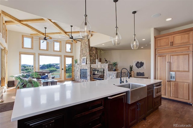 kitchen featuring sink, dark wood-type flooring, paneled refrigerator, a stone fireplace, and a kitchen island with sink