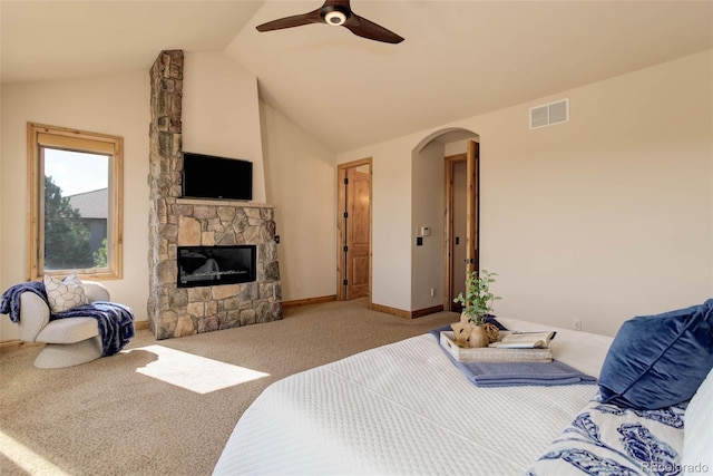 carpeted bedroom with ceiling fan, a stone fireplace, and vaulted ceiling