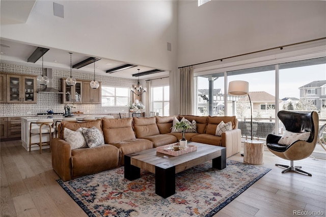 living room with a towering ceiling, a notable chandelier, beam ceiling, and light wood-style floors