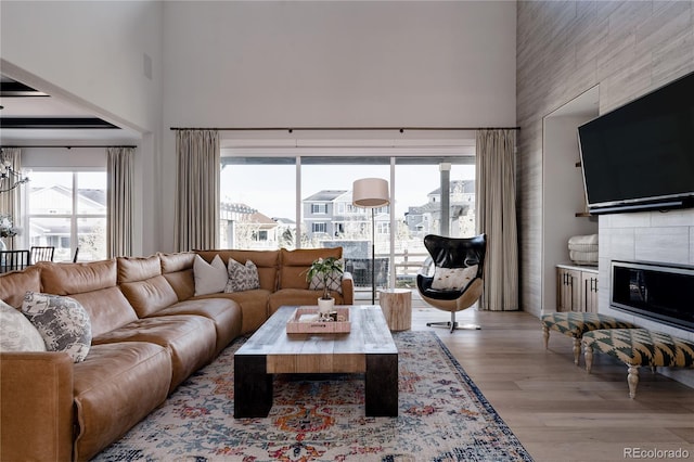 living room with a tiled fireplace, a high ceiling, light wood finished floors, and a chandelier