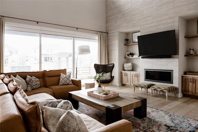living area with a high ceiling, a tile fireplace, built in features, and light wood-type flooring