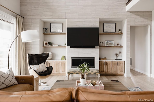 living area featuring a tiled fireplace, light wood finished floors, baseboards, and built in shelves