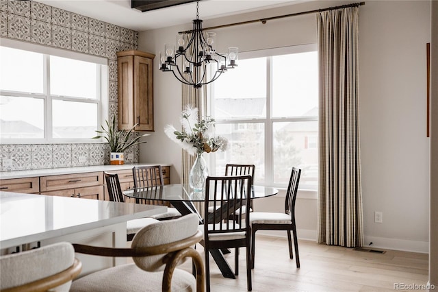 dining space with plenty of natural light, light wood finished floors, baseboards, and a notable chandelier