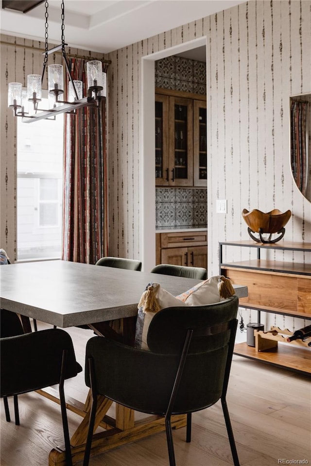 dining area featuring an inviting chandelier, wood finished floors, and wallpapered walls