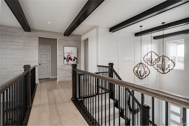 corridor with an inviting chandelier, light wood-style flooring, beam ceiling, and an upstairs landing