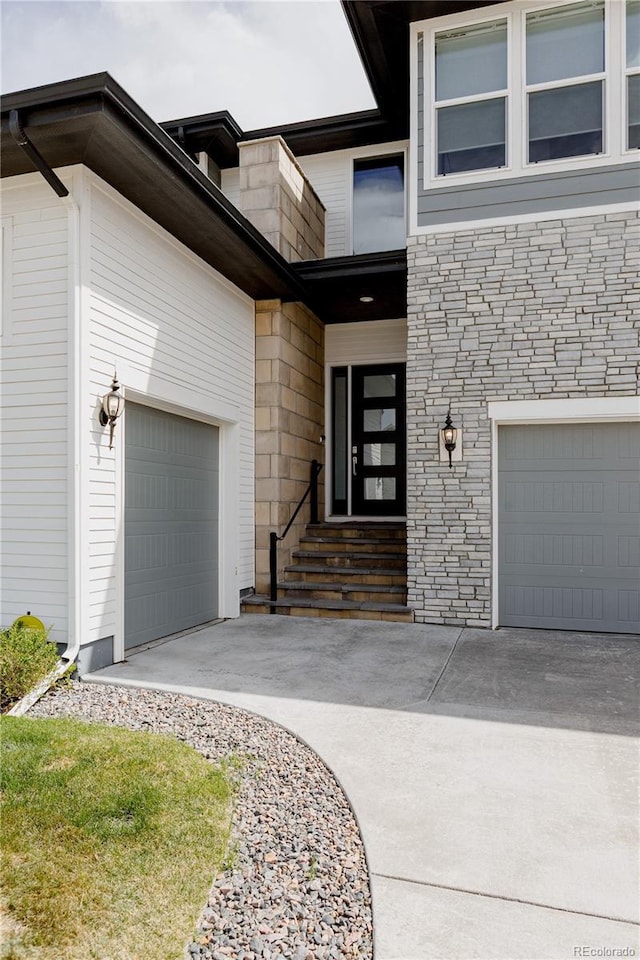 view of exterior entry with concrete driveway, stone siding, and a garage