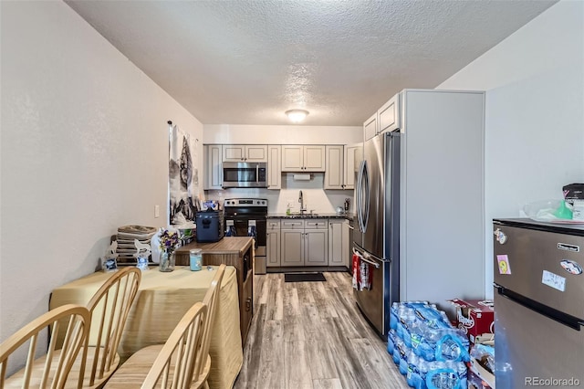 940 S Peoria St, Aurora, CO 80012 - kitchen with stainless steel appliances, a sink, a textured ceiling, light wood-style flooring, and dark countertops