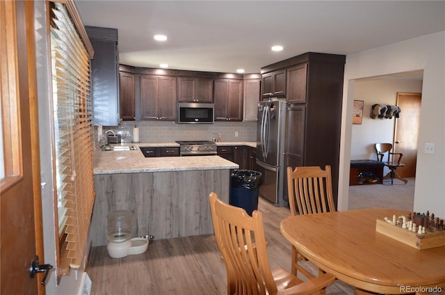 kitchen featuring light wood-style flooring, dark brown cabinetry, a peninsula, appliances with stainless steel finishes, and decorative backsplash