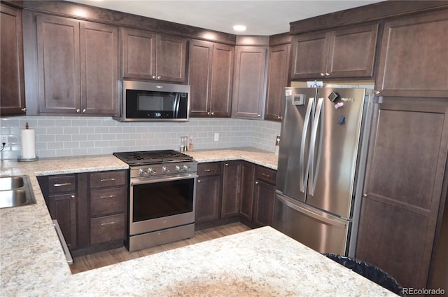 kitchen featuring stainless steel appliances, light wood-style floors, dark brown cabinetry, and tasteful backsplash