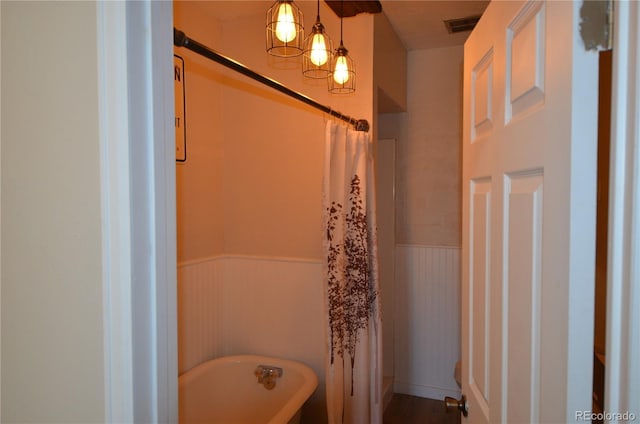 bathroom featuring a wainscoted wall, a freestanding tub, and visible vents