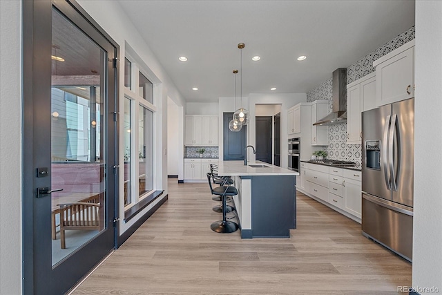 6047 N Nepal Ct, Aurora, CO 80019 - kitchen featuring appliances with stainless steel finishes, wall chimney exhaust hood, white cabinetry, light wood-style flooring, and backsplash