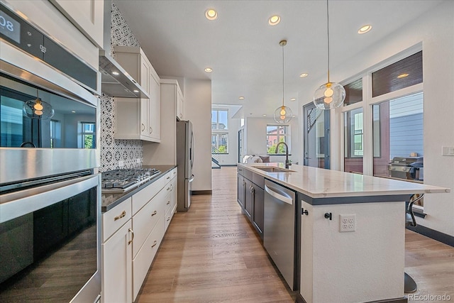 6047 N Nepal Ct, Aurora, CO 80019 - kitchen featuring stainless steel appliances, white cabinetry, an island with sink, light wood finished floors, and decorative backsplash