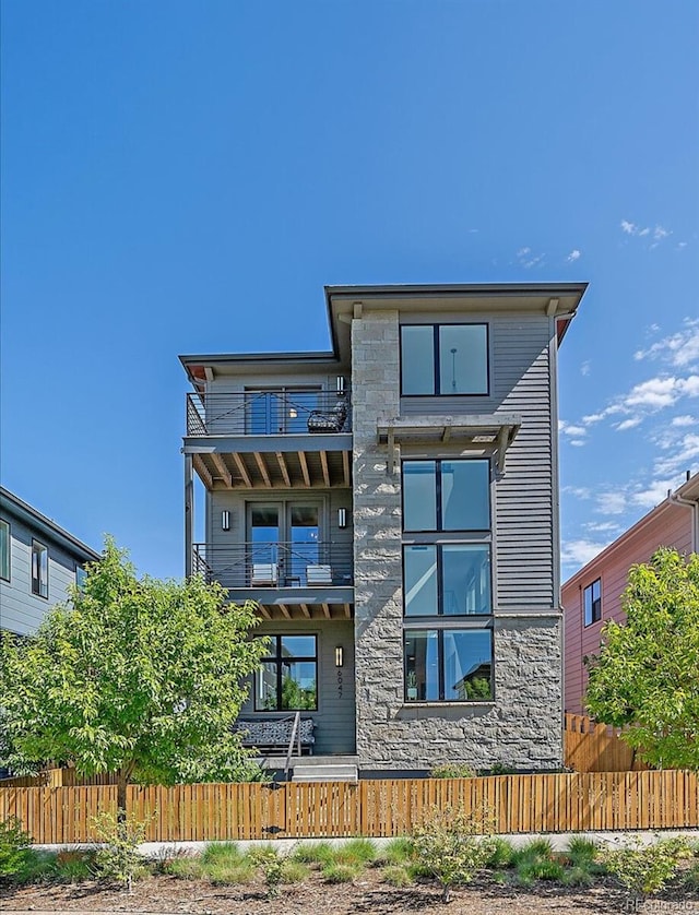 6047 N Nepal Ct, Aurora, CO 80019 - rear view of property with a balcony, a fenced front yard, and stone siding