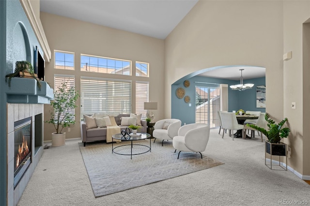 carpeted living area with baseboards, a chandelier, a towering ceiling, arched walkways, and a glass covered fireplace