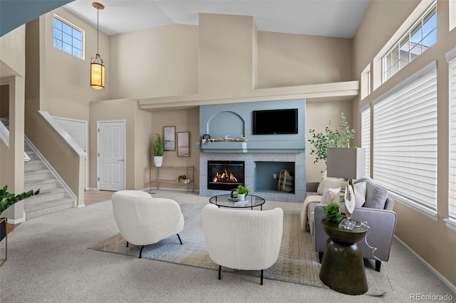 carpeted living room featuring a tiled fireplace, stairway, baseboards, and high vaulted ceiling