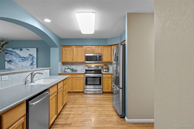 kitchen with decorative backsplash, light wood-style floors, a textured wall, stainless steel appliances, and a sink