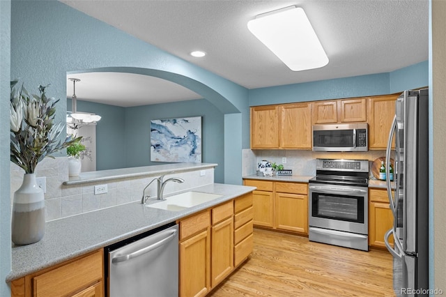 kitchen with a sink, backsplash, light wood-style floors, appliances with stainless steel finishes, and light countertops