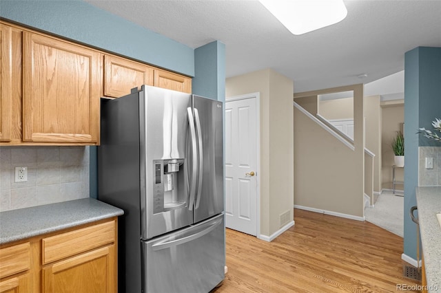 kitchen featuring baseboards, light wood finished floors, light countertops, stainless steel refrigerator with ice dispenser, and tasteful backsplash