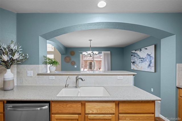 kitchen with arched walkways, stainless steel dishwasher, light countertops, and a sink