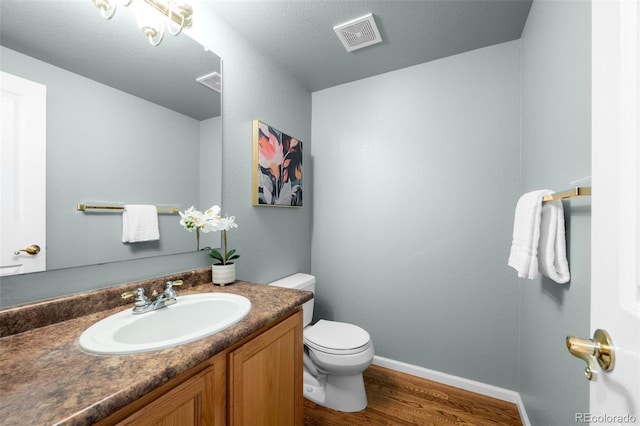 half bath with visible vents, baseboards, toilet, wood finished floors, and vanity