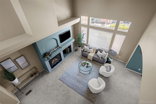 living area featuring visible vents, baseboards, a towering ceiling, a glass covered fireplace, and carpet flooring