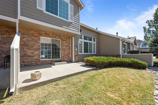 view of exterior entry with a yard, brick siding, and a patio area